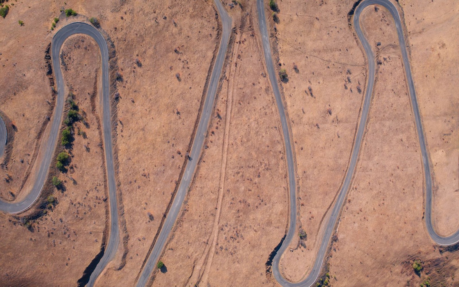 Aerial view of a switchback road winding across dry, hilly terrain